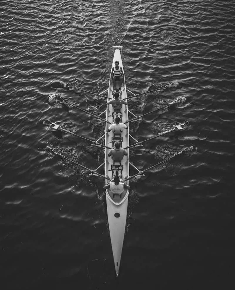 A rowing crew moving as one, with one person setting the rhythm from the back of the boat